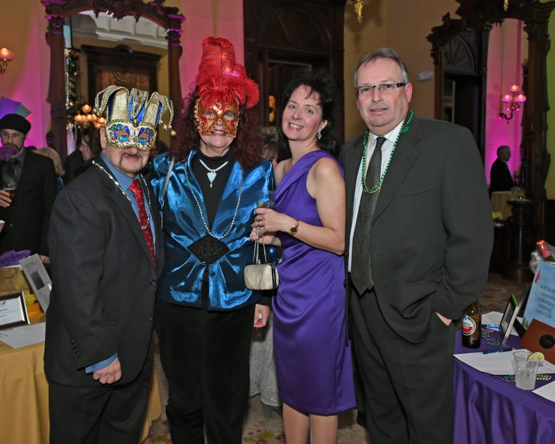 Group of four people, two with masks on, at Mardi Gras for AIM Services