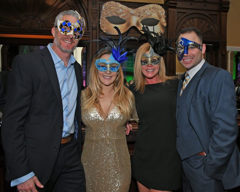 Group of four people with mardi gras masks on smiling at Mardi Gras for AIM Services